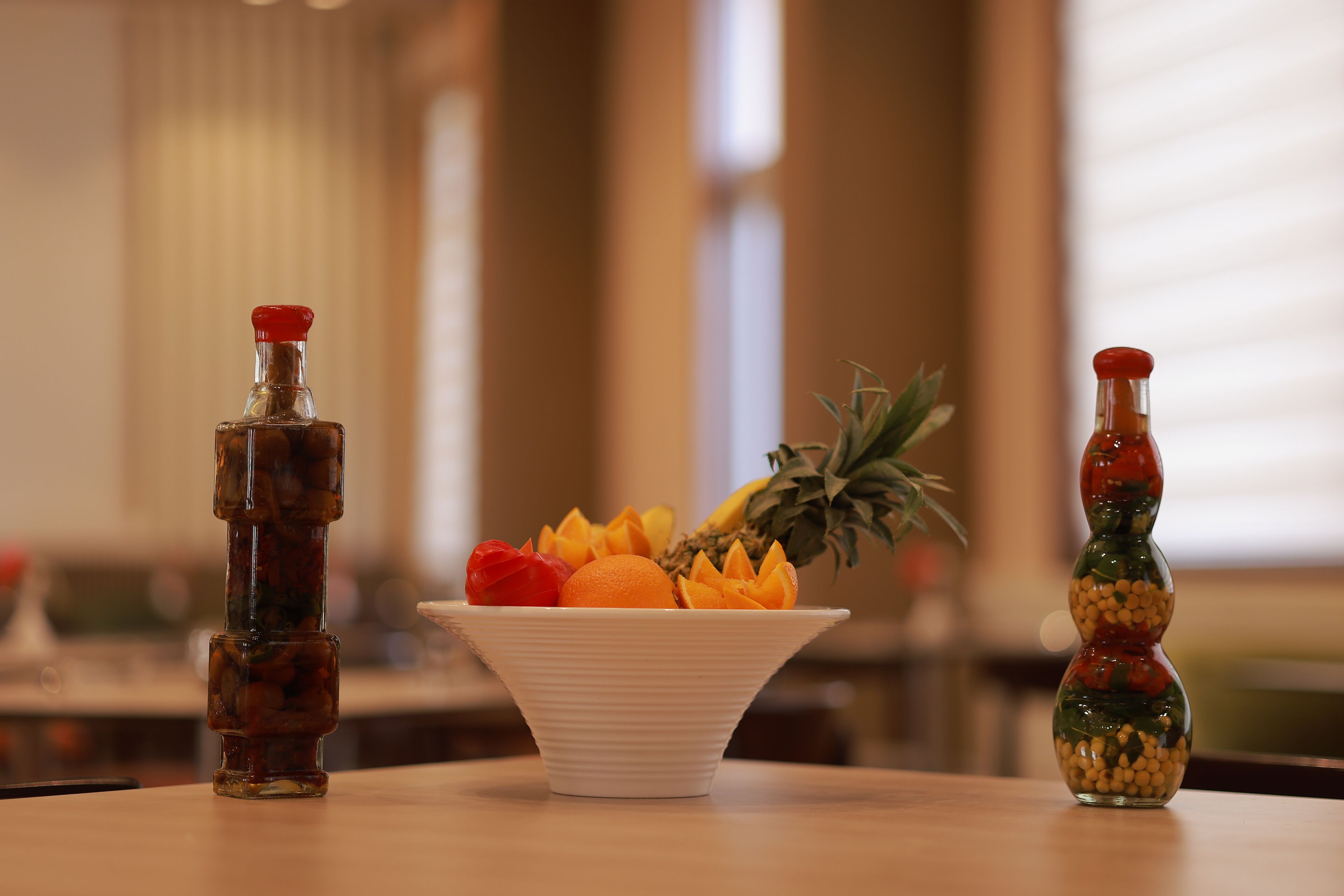 Una mesa con un bol blanco que contiene fruta y dos botellas de salsa.