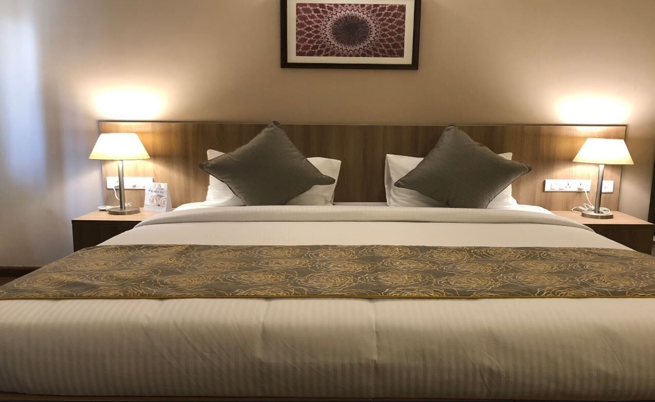 A hotel room with a large bed, two bedside lamps, a framed artwork above the bed, and a patterned bedspread.