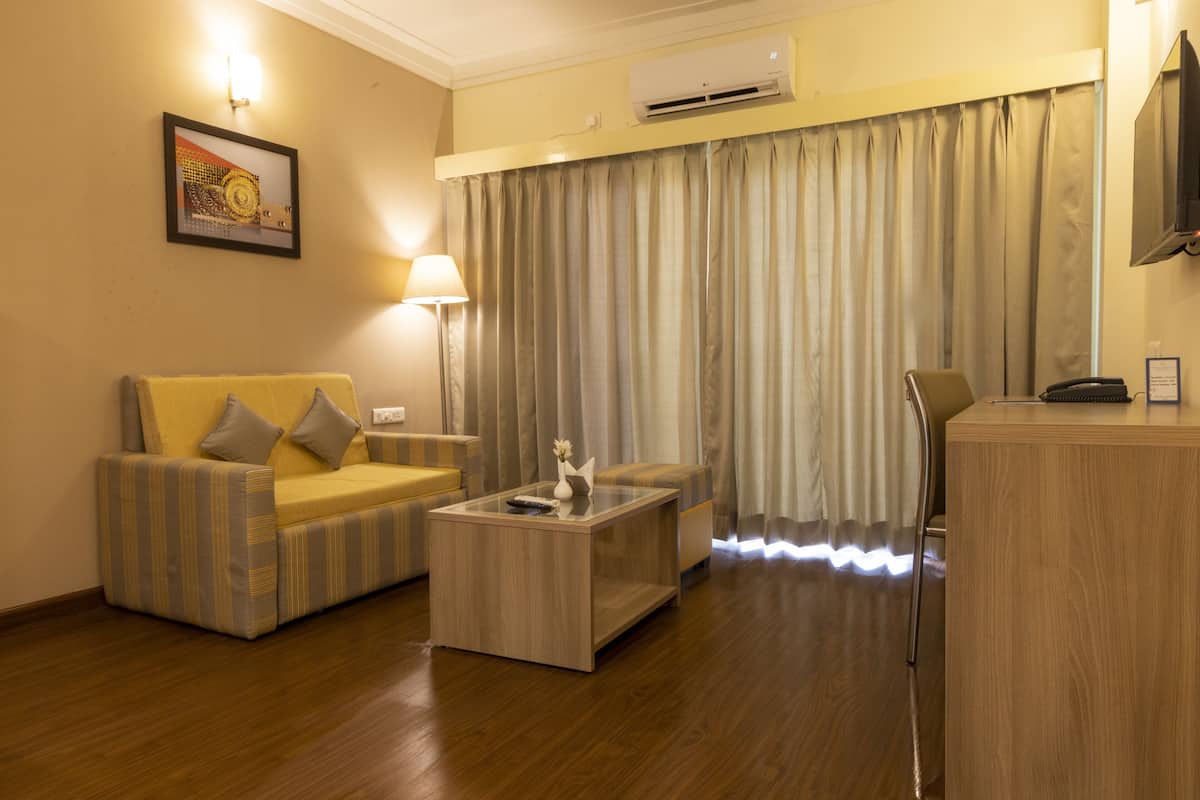 Quarto de hotel com sofá, mesa de centro, luminária, ar condicionado e televisão.
