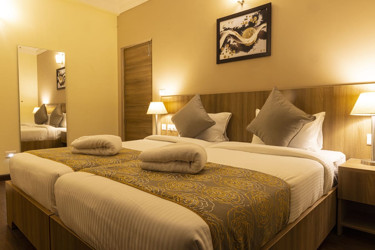 Quarto de hotel com uma cama grande, luminárias de cabeceira, um espelho e uma obra de arte emoldurada na parede.