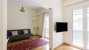 A living room with a dark sofa, a patterned rug, a green pendant light, and a TV mounted on the wall. - ★ Bright & Spacious 2-bedroom Apartment in Athens (Athens)