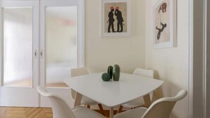 A dining area with a white table and chairs, two framed pictures on the wall, and a door with blinds. - ★ Bright & Spacious 2-bedroom Apartment in Athens (Athens)