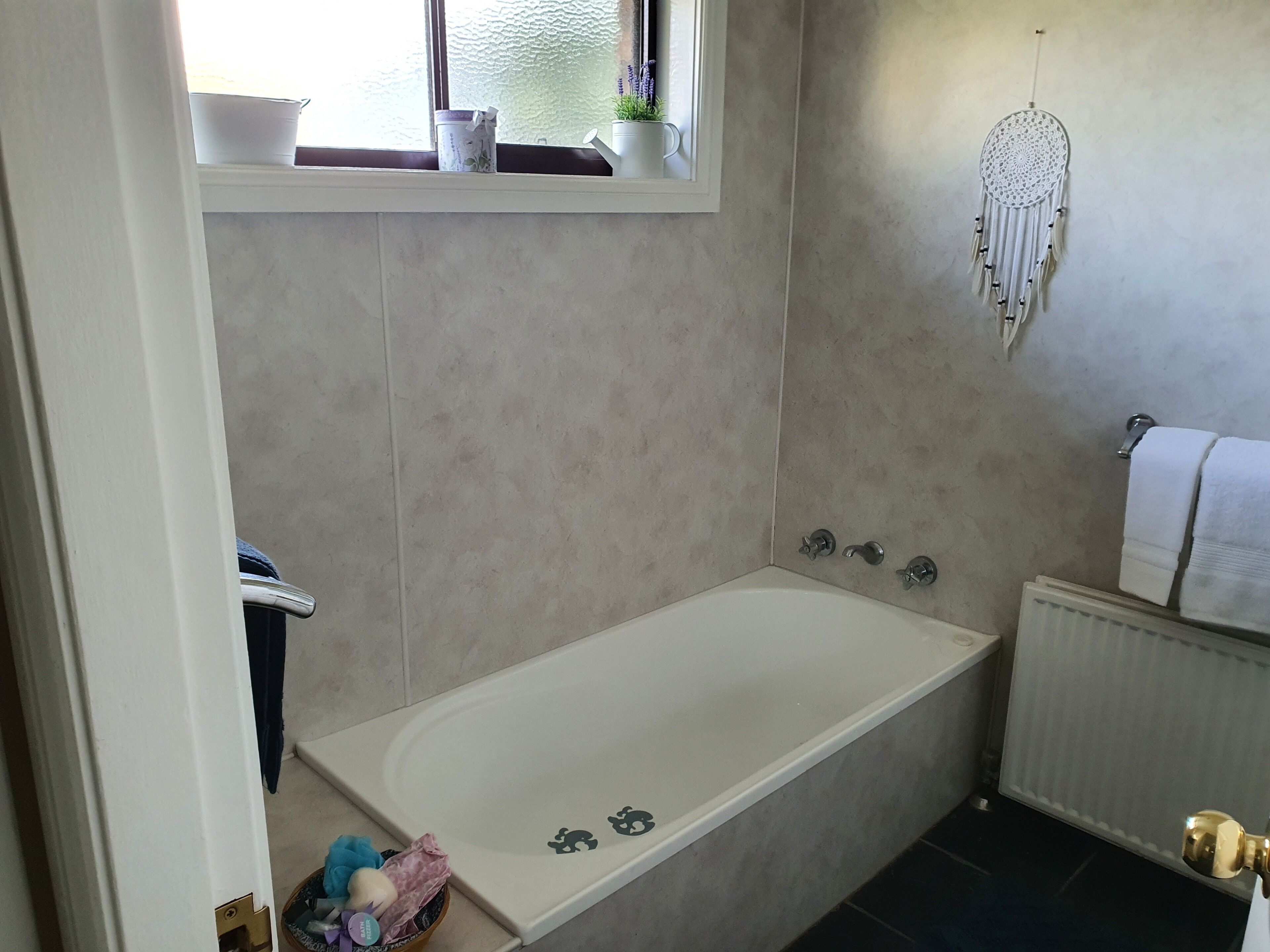 Une salle de bain avec une baignoire, une fenêtre ornée de plantes, un attrape-rêves et un porte-serviettes.