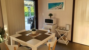 A dining area with a white table, four chairs, a small potted plant, and a microwave on a white cabinet. - The Junction Estate. Cool, Calm and Cozy. (Wallerawang)