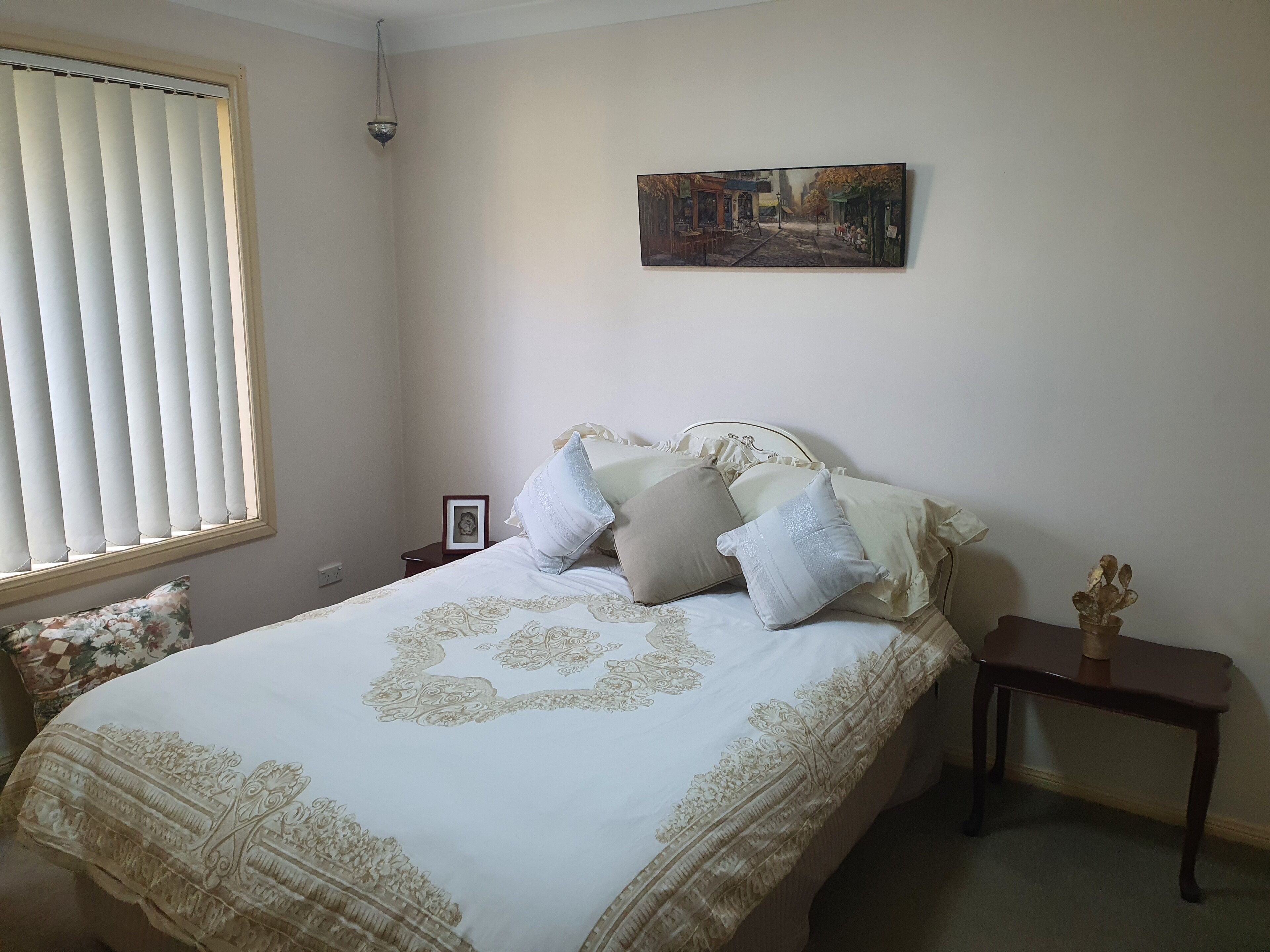 Une chambre à coucher avec un lit, une table de chevet, un cadre photo et une fenêtre avec des stores.