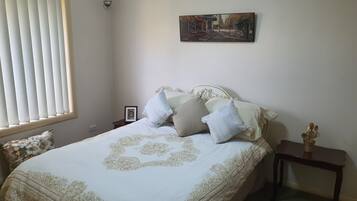 Ein Schlafzimmer mit Bett, Nachttisch, Bilderrahmen und Fenster mit Jalousien.