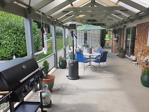 En täckt uteplats med en grill, utemöbler och krukväxter.