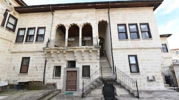 A historic building with a central balcony, stone facade, and a staircase leading to the entrance.