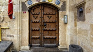 A large wooden double door with a metal handle, flanked by stone walls and a small window. - Kadievi (Ürgüp)