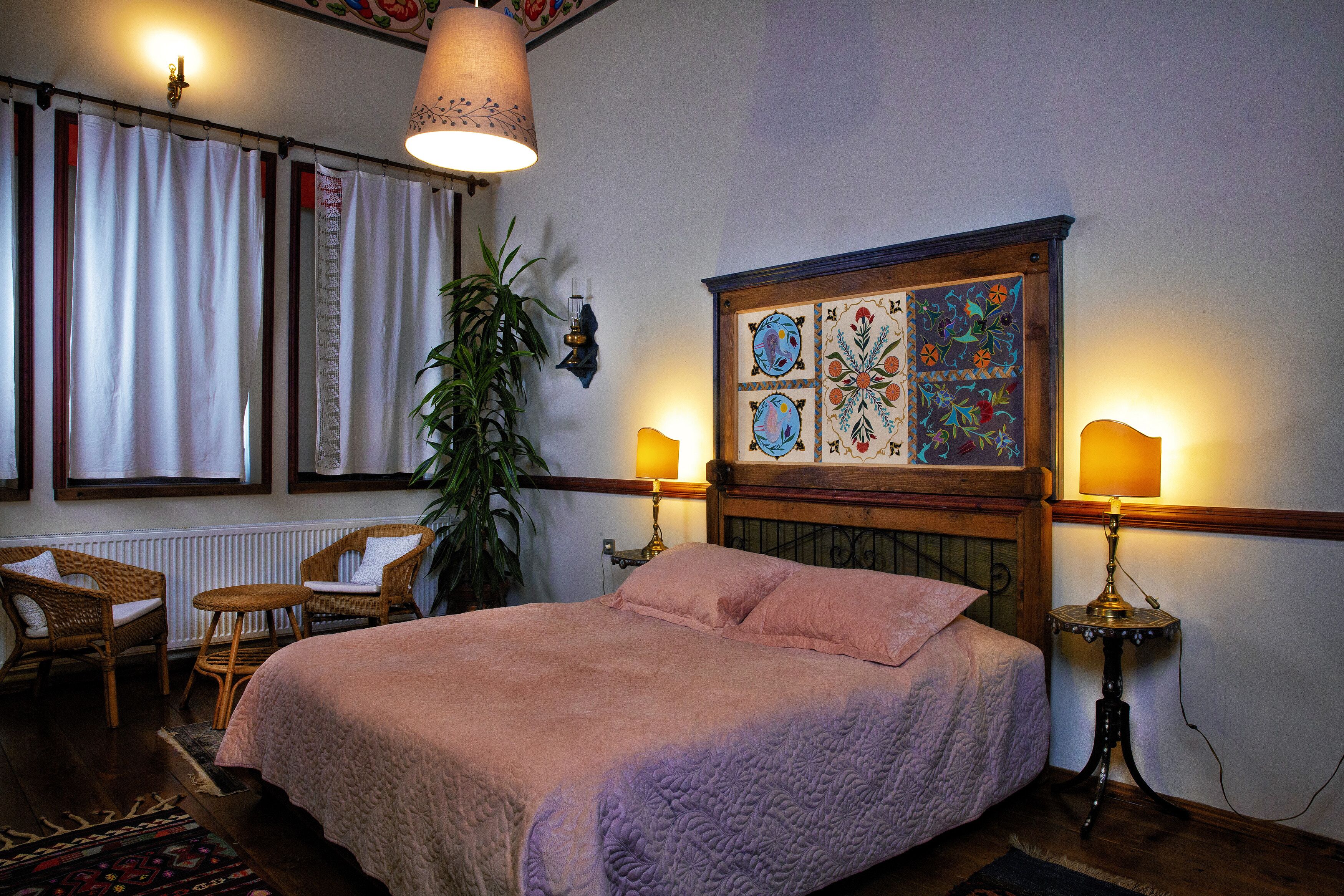 Un dormitorio con una cama, dos sillas, una mesa, una planta en maceta y un panel decorativo en la pared.