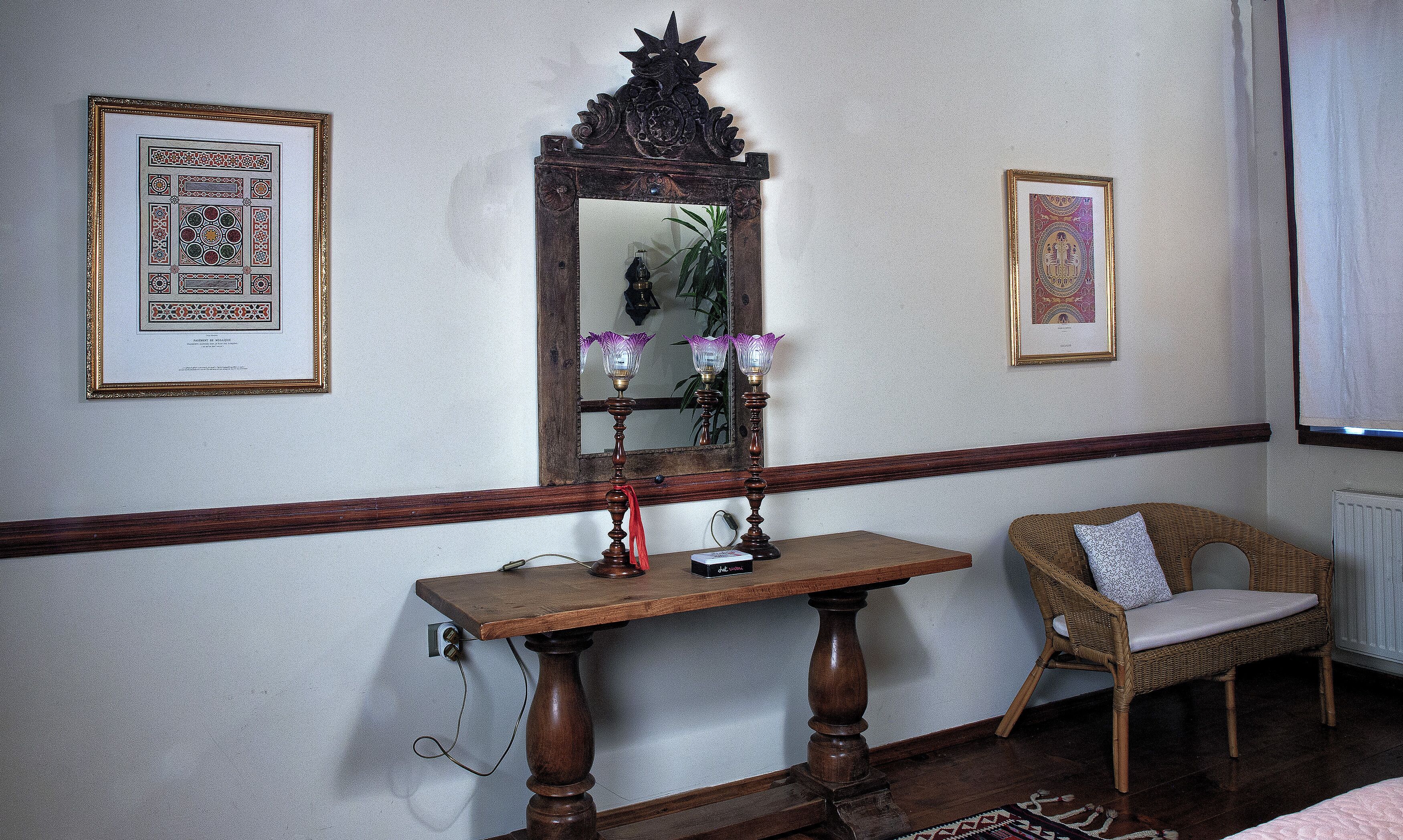 Una habitación con una mesa de madera, una silla de mimbre, un espejo y cuadros en las paredes.