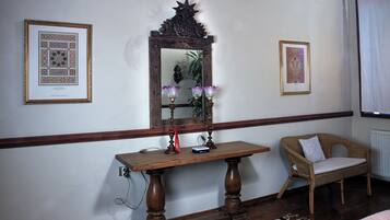 Una habitación con una mesa de madera, una silla de mimbre, un espejo y cuadros en las paredes.