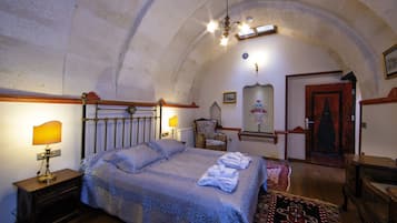 A bedroom with a bed, two bedside lamps, a chair, a door, and a chandelier.