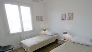 A simple, clean room with two single beds, a chair, and a small table with a lamp. - Charming Renovated House: Close to Beach & Town Center, Modern Amenities (La Tranche-sur-Mer)