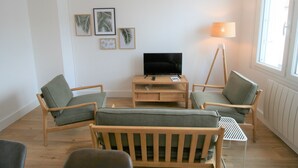 A living room with a TV, wooden furniture, and framed pictures on the wall. - Charming Renovated House: Close to Beach & Town Center, Modern Amenities (La Tranche-sur-Mer)