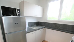 A compact kitchen with a stainless steel refrigerator, a microwave, a sink, and white cabinets. - Charming Renovated House: Close to Beach & Town Center, Modern Amenities (La Tranche-sur-Mer)