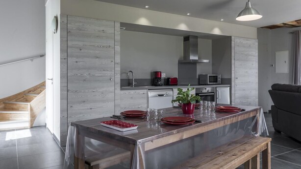 Une cuisine moderne avec un banc en bois, une table à manger dressée avec des assiettes rouges et un grand miroir au-dessus de l’évier.