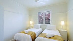 A hotel room with two single beds, each with a white blanket and a rolled towel. There are two bedside tables with lamps, and a window with blinds. - The Byron Pavilion - Nestled in the heart of Byron, park the car and walk everywhere. (Byron Bay)