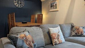 Un salon moderne avec un canapé gris, une table à manger en bois et une horloge murale.