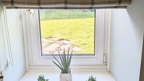 Une fenêtre donnant sur un champ verdoyant, un rebord de fenêtre blanc et deux plantes en pot.