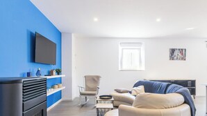 A modern living room with a sofa, armchair, and a flat-screen TV mounted on a blue wall. - Modern house with bikes, near Sartilly trails (Sartilly)