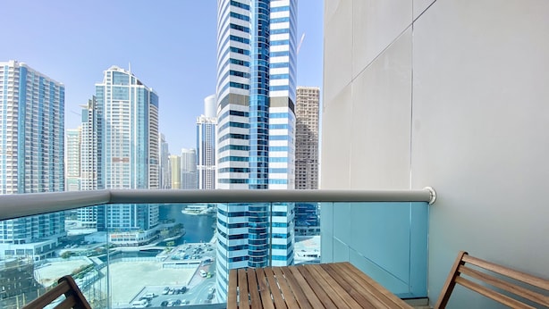 Een balkon met een houten tafel en stoelen, met uitzicht op een stadsbeeld met moderne wolkenkrabbers.