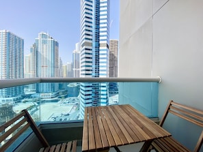 A balcony with a wooden table and chairs, overlooking a cityscape with modern high-rise buildings.