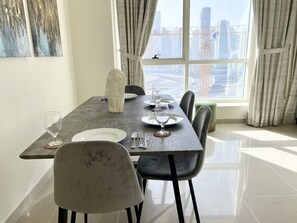 A dining area with a table set for four, a vase, and a view of a cityscape through large windows.