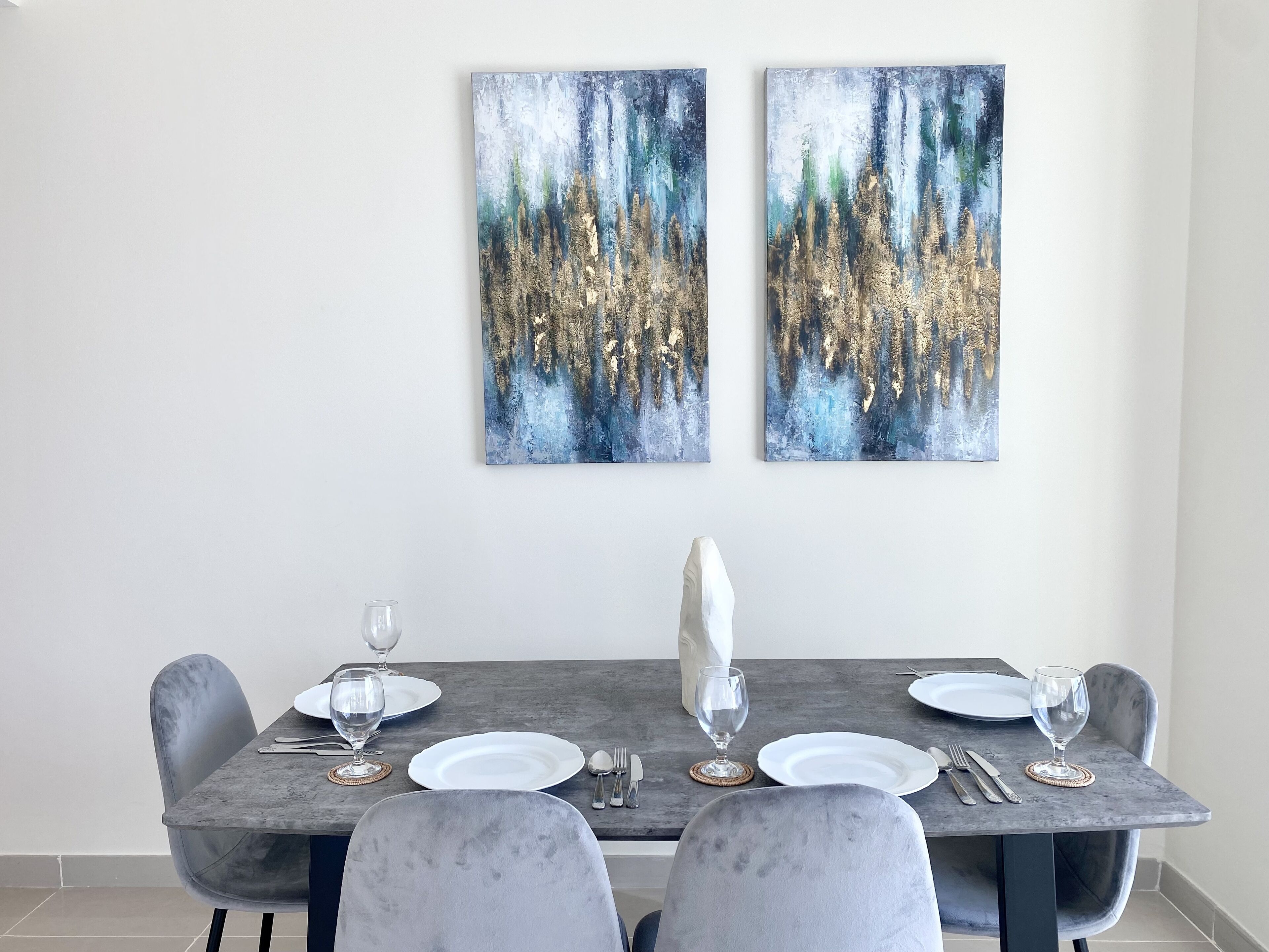 A dining area with a gray marble table, two gray chairs, and two abstract paintings on the wall.