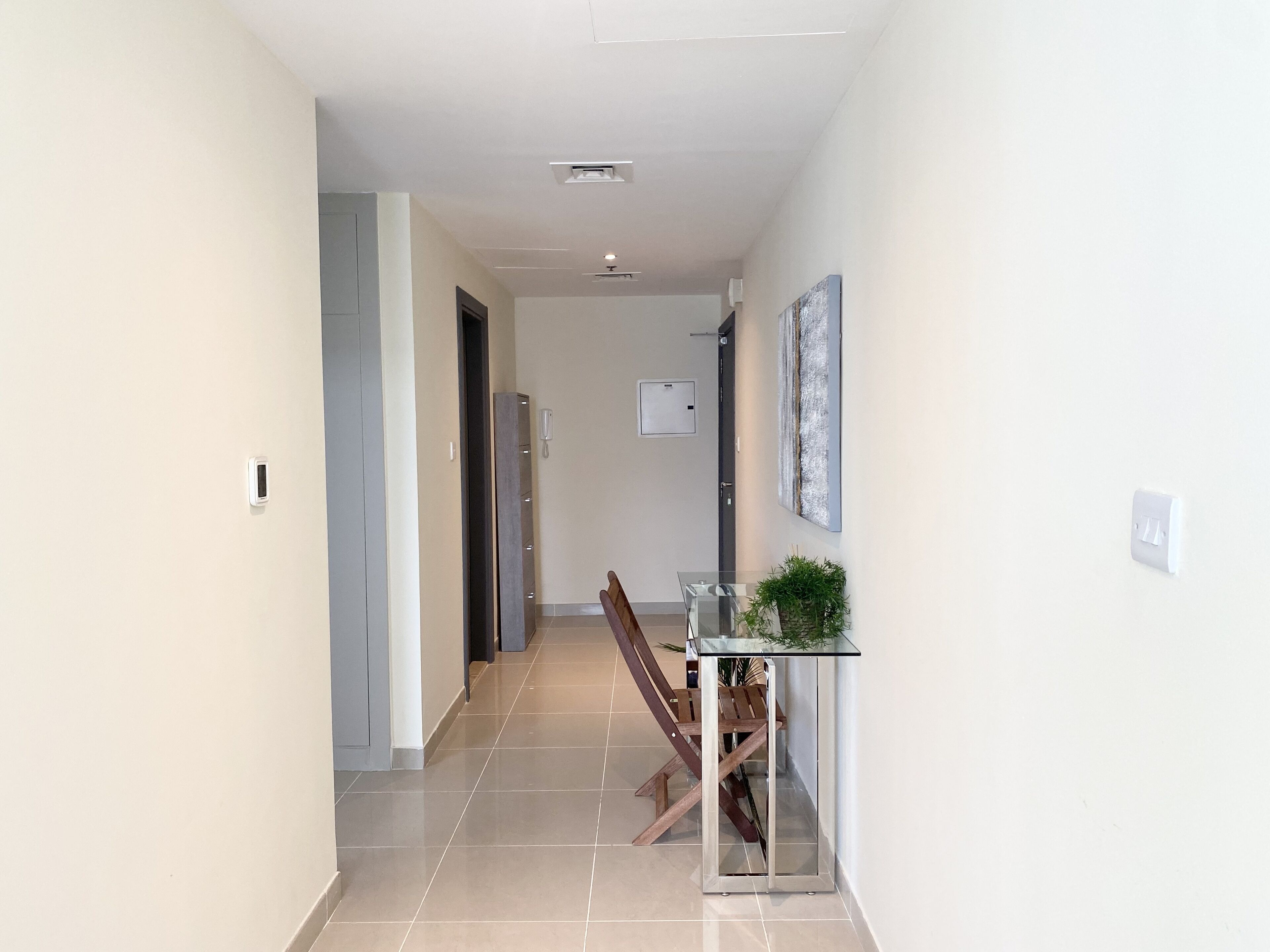 A hallway with a glass-top table and chairs, a wall-mounted phone, and a door leading to another room.