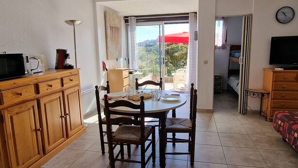 Un coin repas avec une table et des chaises, une cuisine équipée d’un four à micro-ondes et d’un grille-pain, et un téléviseur dans une chambre.