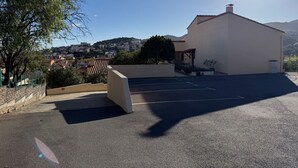 Un espace de stationnement avec un bâtiment en arrière-plan, un ciel dégagé et une vue lointaine d’une ville.