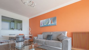 A modern living room with a grey sofa, a glass coffee table, and a dining area with a glass table and chairs. - Modern 80m² apartment with wifi, dishwasher, balcony, and sea view (Les Sables-d'Olonne)