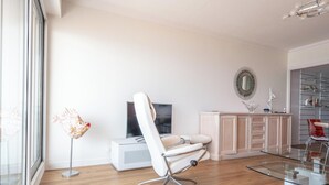 A modern living room with a white leather sofa, a glass coffee table, and a television on a white stand. - Modern 80m² apartment with wifi, dishwasher, balcony, and sea view (Les Sables-d'Olonne)