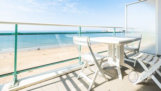 A balcony with a glass railing overlooking a beach. There is a table and two chairs. - Modern 80m² apartment with wifi, dishwasher, balcony, and sea view (Les Sables-d'Olonne)