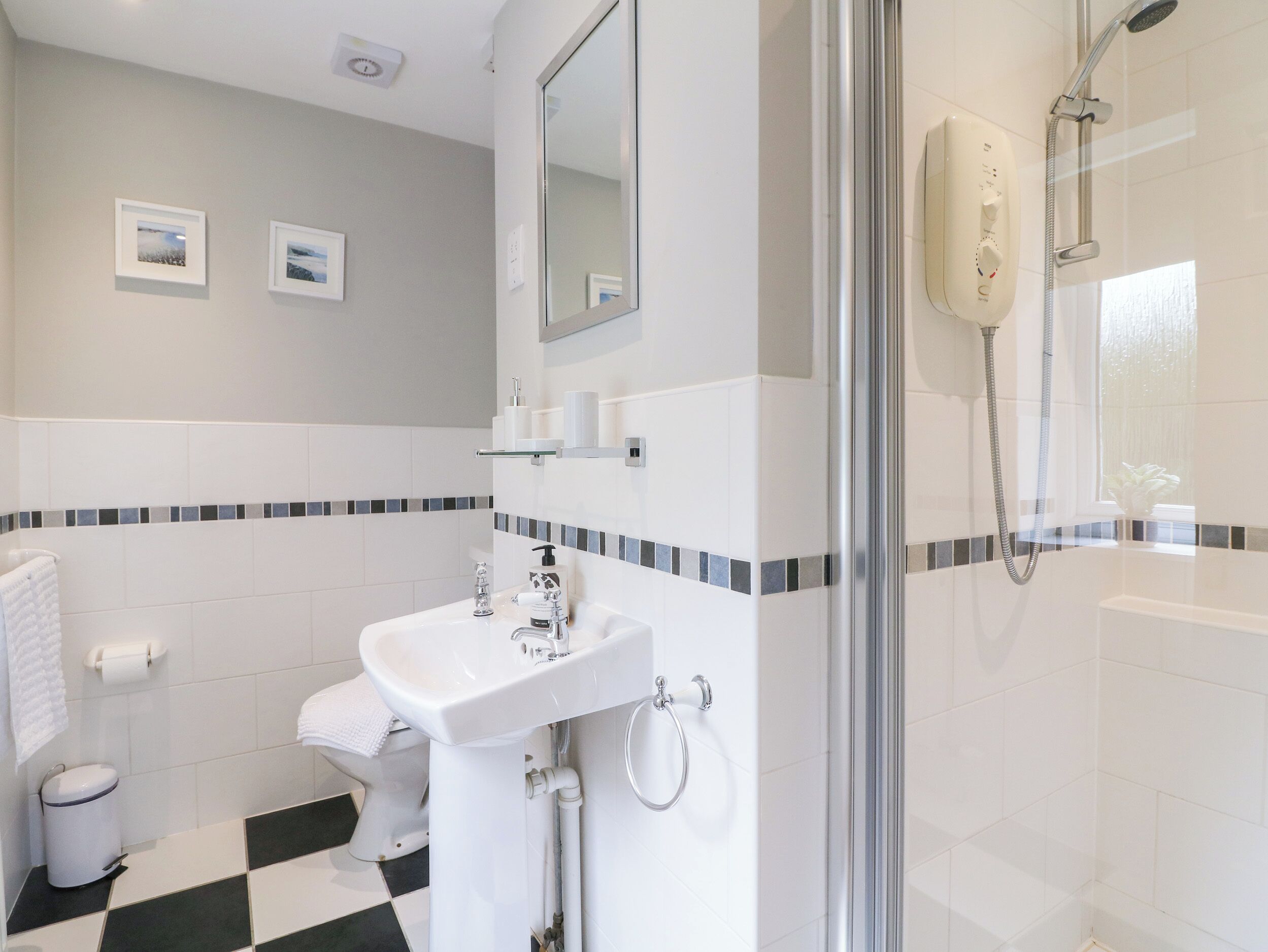 Un baño con lavamanos, inodoro y ducha. Hay cuadros enmarcados en la pared y una ventana con vistas.
