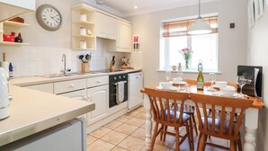 Een moderne keuken met witte kasten, een inbouwoven en een eethoek met houten stoelen en een tafel.