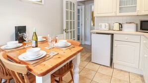Een kleine keuken met witte kasten, een compacte koelkast en een eethoek met een houten tafel gedekt voor twee personen.
