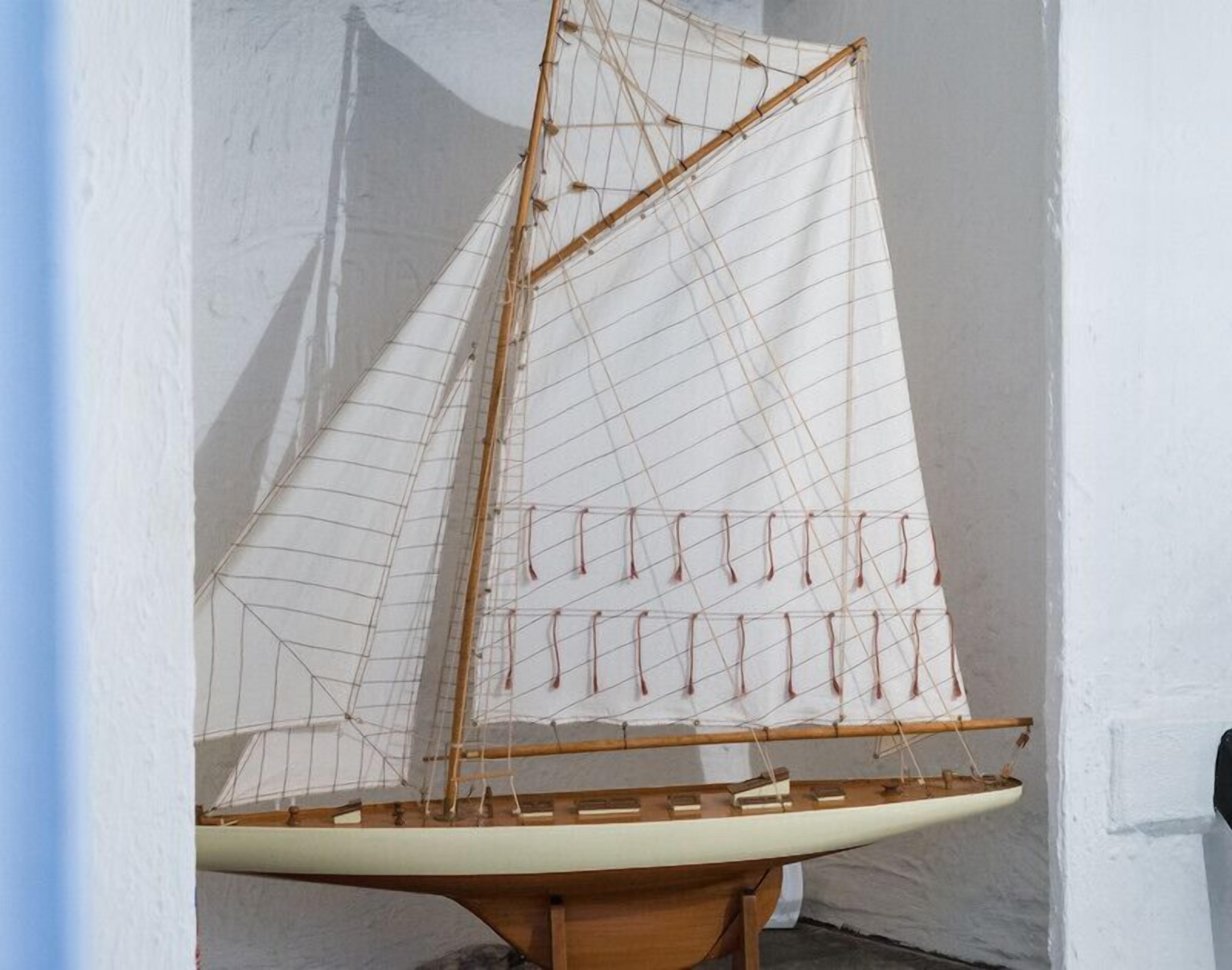 Ein Modellsegelschiff mit Holzkörper und Segeln, präsentiert in Innenräumen.