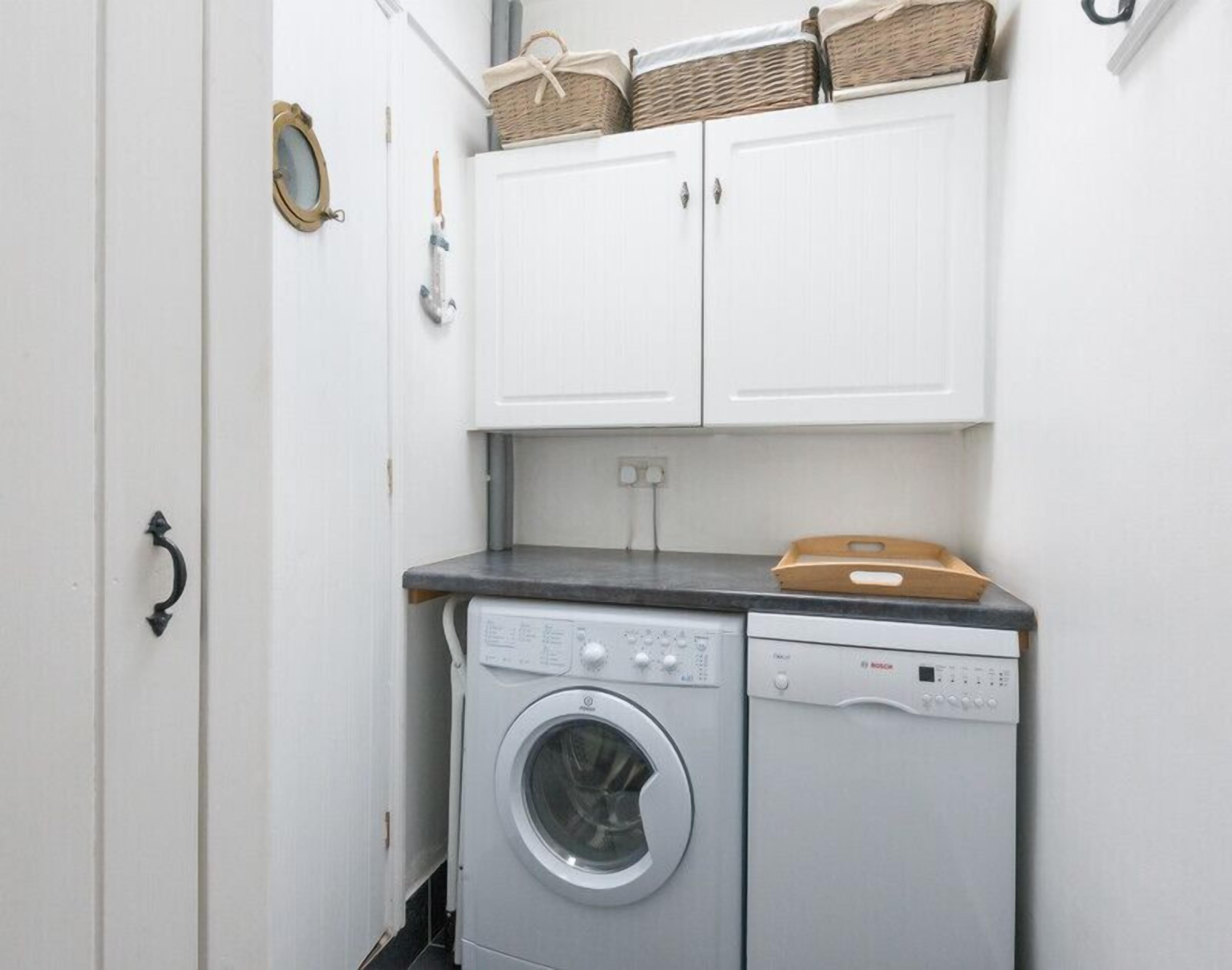 A laundry room with a washing machine and dryer, white cabinets above, and baskets on top.