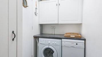A laundry room with a washing machine and dryer, white cabinets above, and baskets on top.