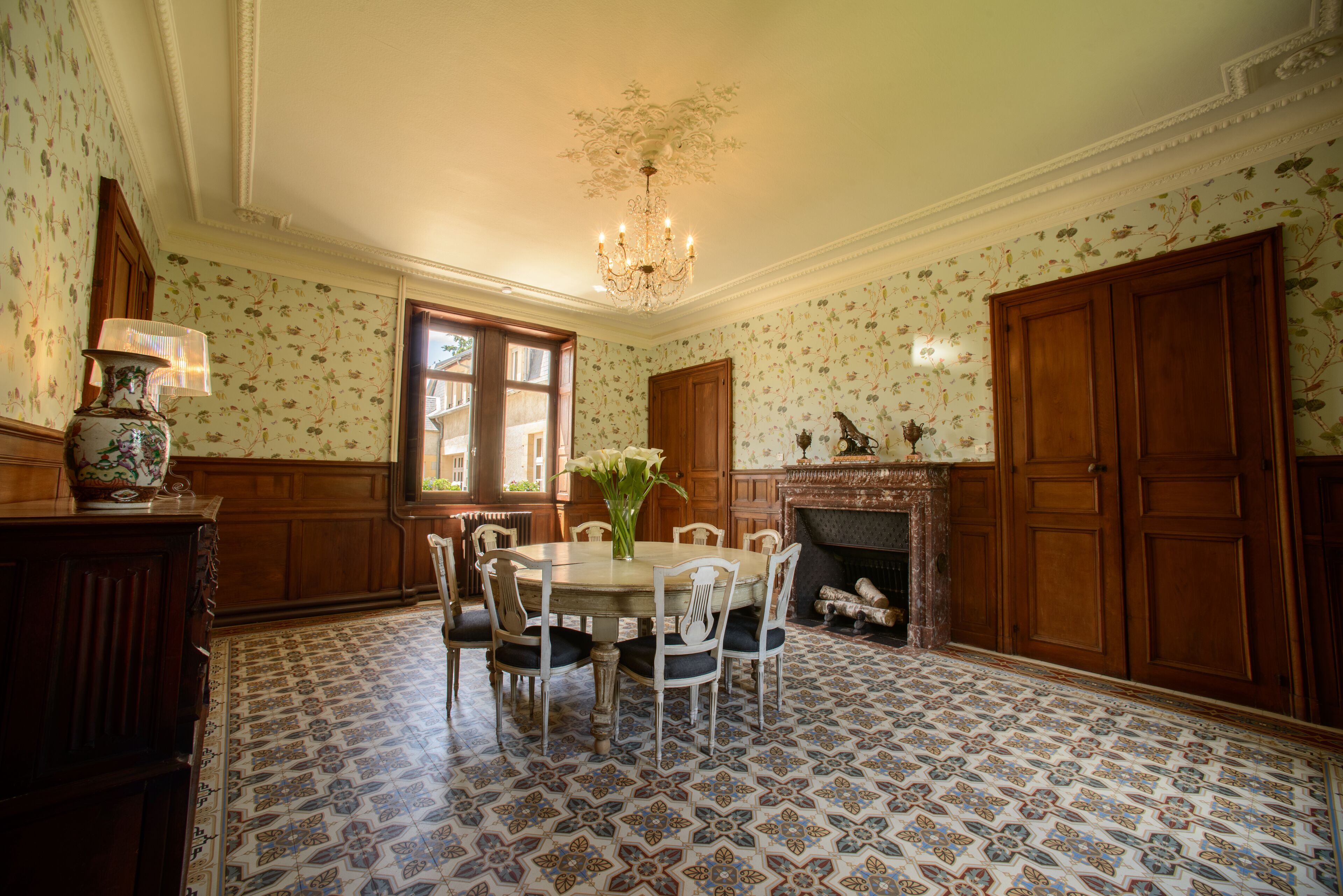 Uma sala de jantar com uma mesa redonda, cadeiras, um lustre e uma lareira.