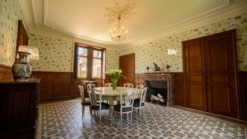 Uma sala de jantar com uma mesa redonda, cadeiras, um lustre e uma lareira.
