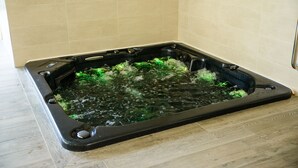 Un bain à remous rectangulaire doté d’un bord noir, entouré de murs recouverts de carreaux beiges et d’un plancher en bois.