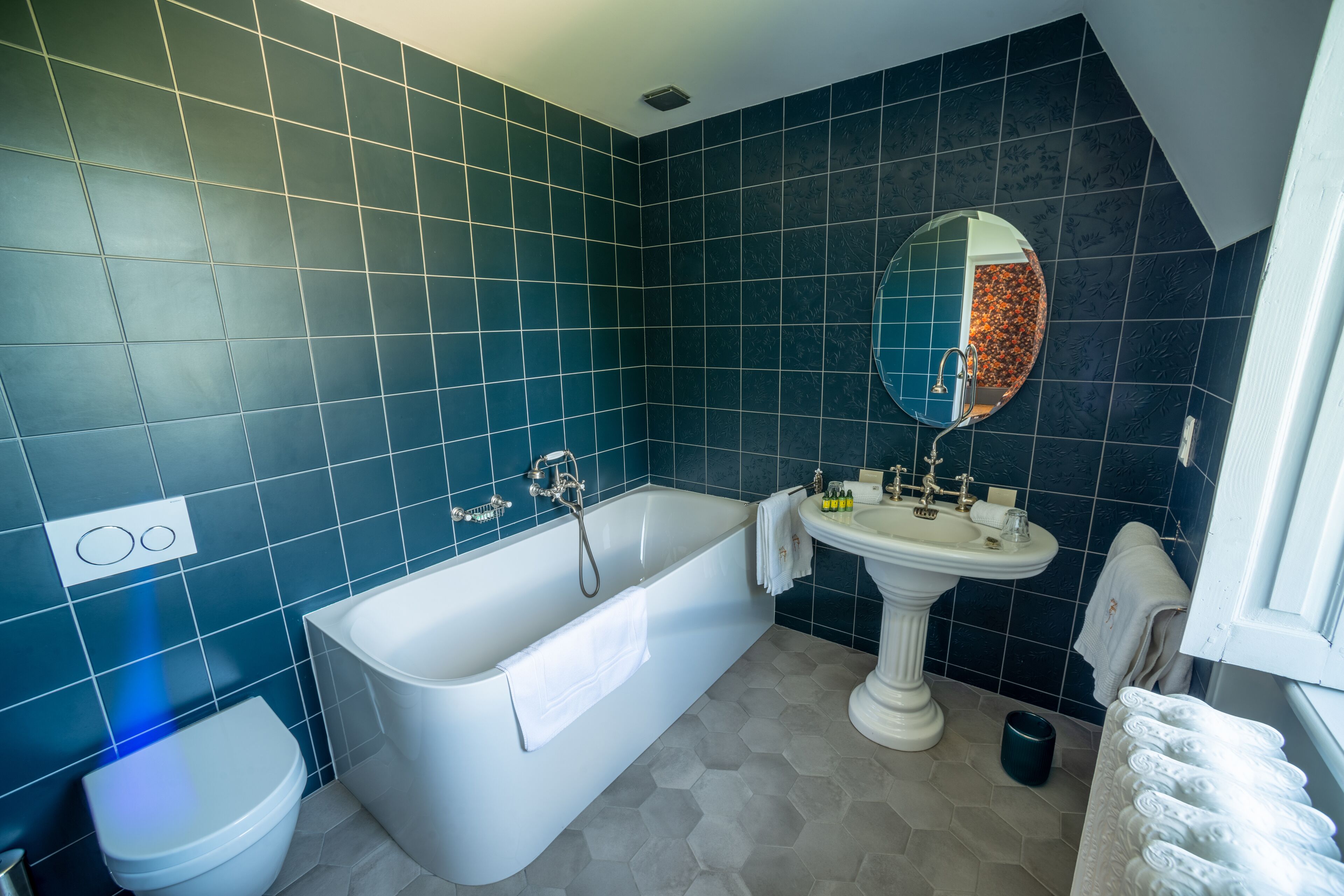 Een badkamer met een bad, wastafel en toilet, met blauwe en grijze tegels.
