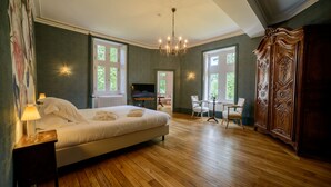 Une chambre avec un grand lit, un plancher en bois, un lustre, une armoire en bois et une vue sur l’extérieur par les fenêtres.