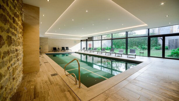 Une piscine intérieure moderne, avec un mur en pierre, un plancher en bois et une vue sur l’extérieur.