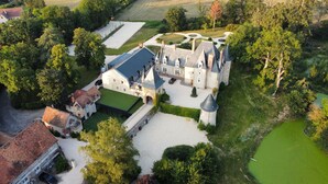 Vue aérienne d’un château doté de nombreuses tours, d’une vaste cour et entouré de verdure.