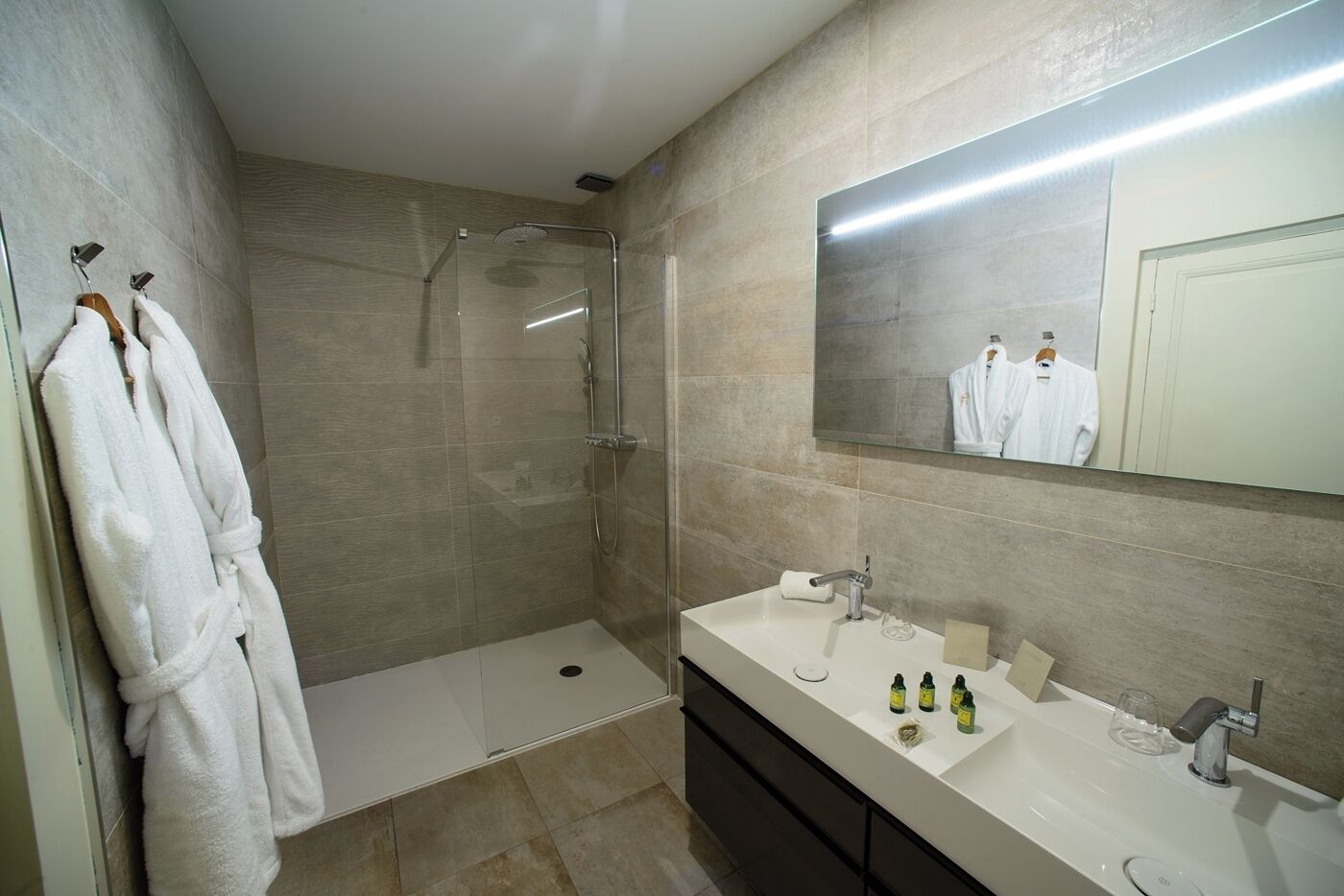 A modern bathroom with a glass-enclosed shower, a white bathtub, and a vanity with a large mirror.
