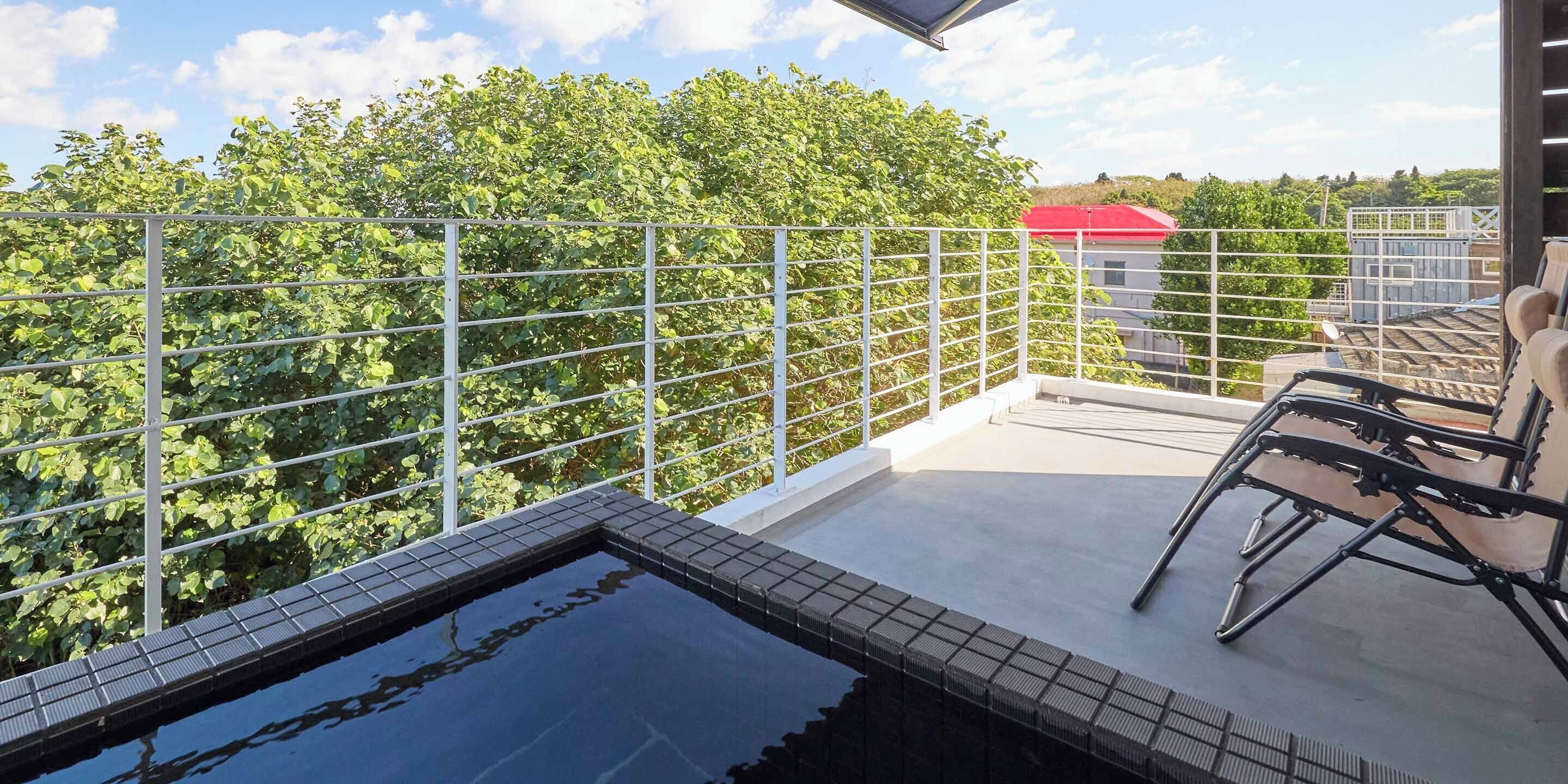 A rooftop terrace with a swimming pool, a metal railing, and a view of trees and buildings.